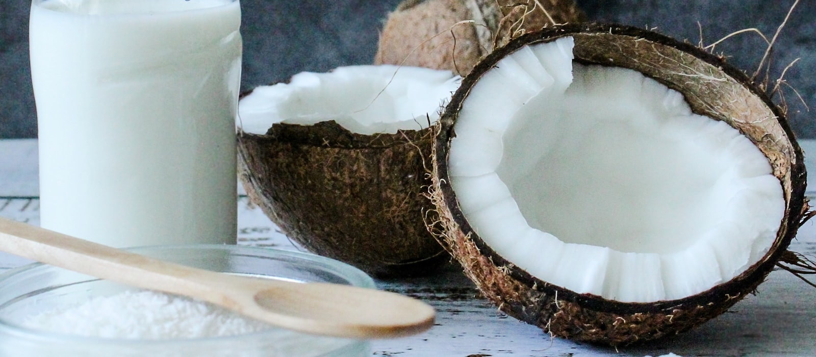 A split coconut beside a jar of coconut oil and a bottle of coconut milk