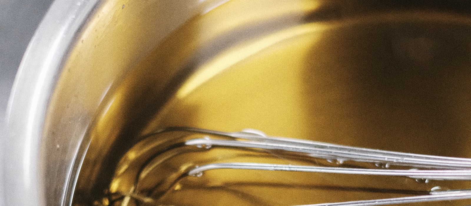 A whisk resting in a saucepan of melted golden butter