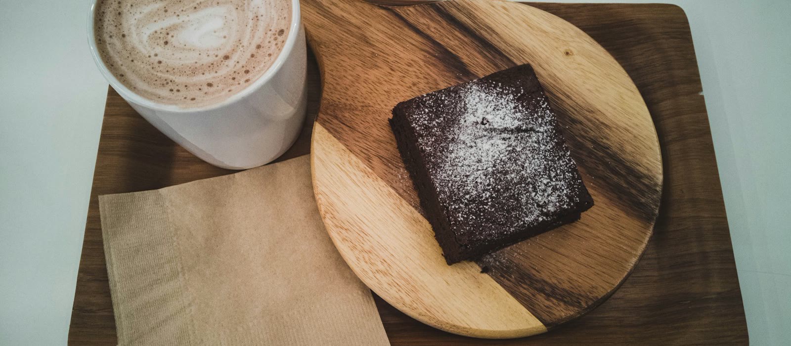 A brownie and a latte on a wooden serving board