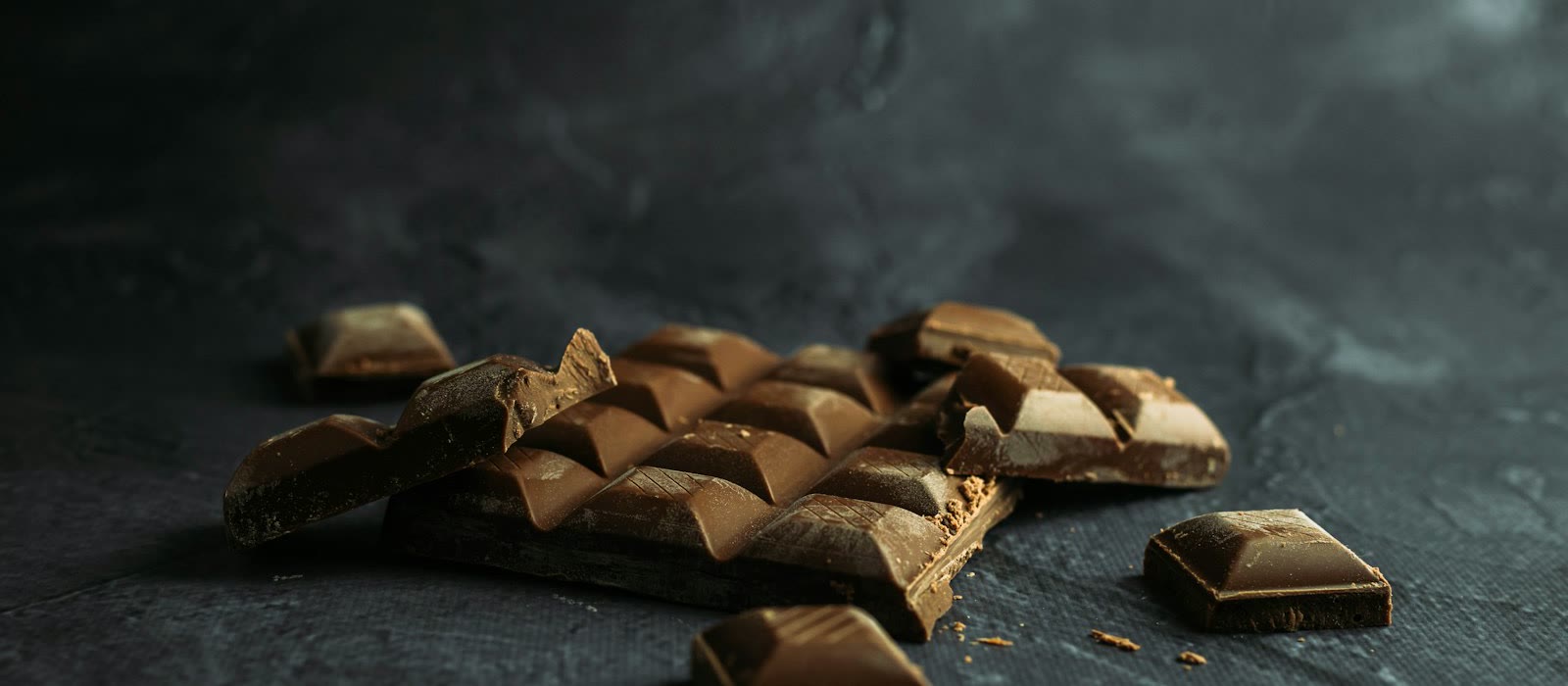 A dark chocolate bar broken into small squares on a slate surface