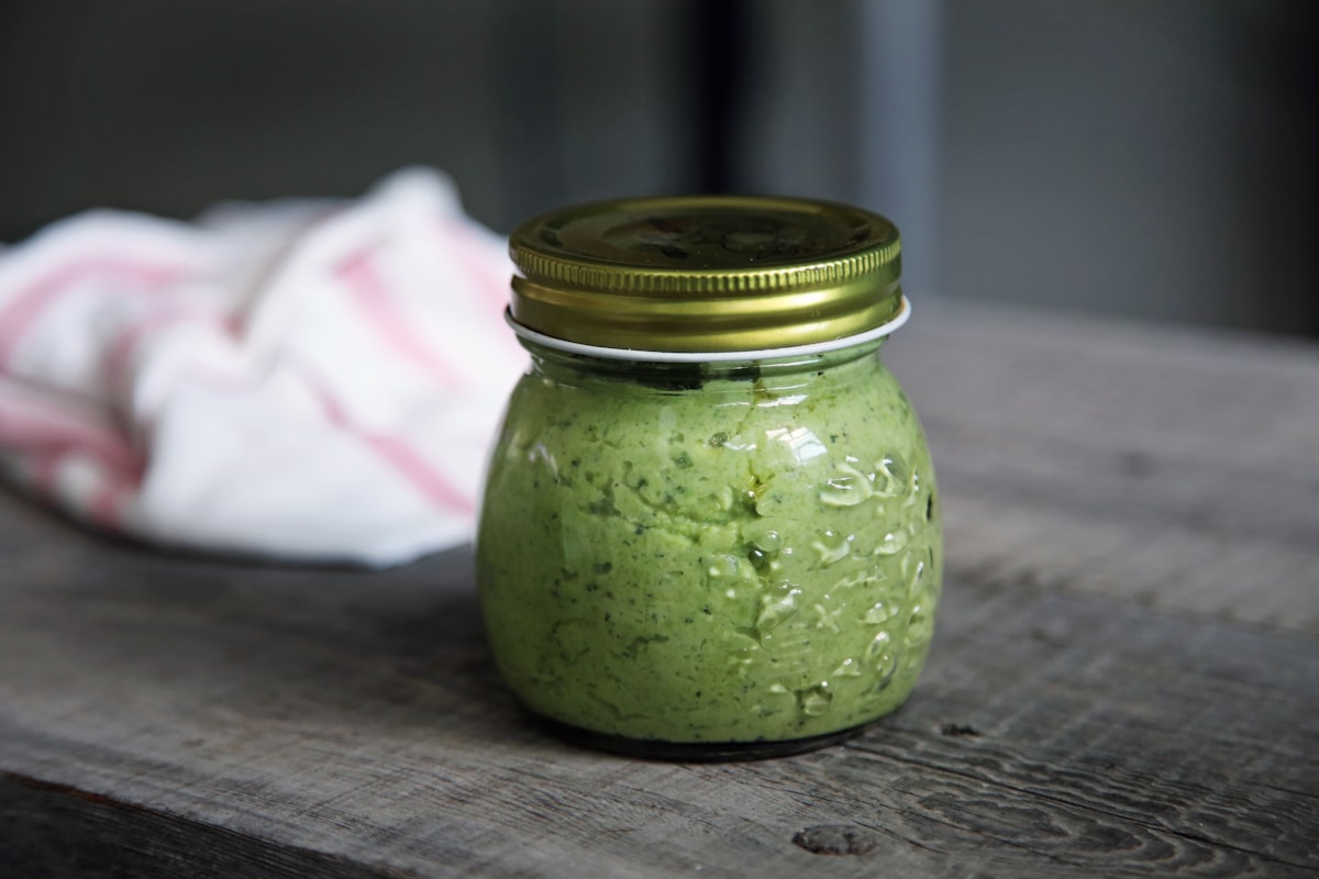 A jar of green basil pesto on a grey surface