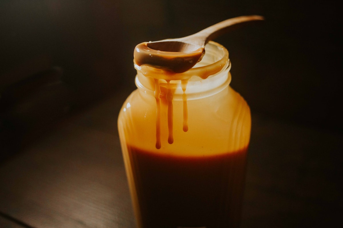 Glossy caramel sauce dripping from a spoon into a glass jar