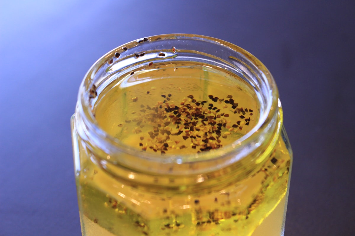 An open glass jar of golden chili oil with flakes floating on top