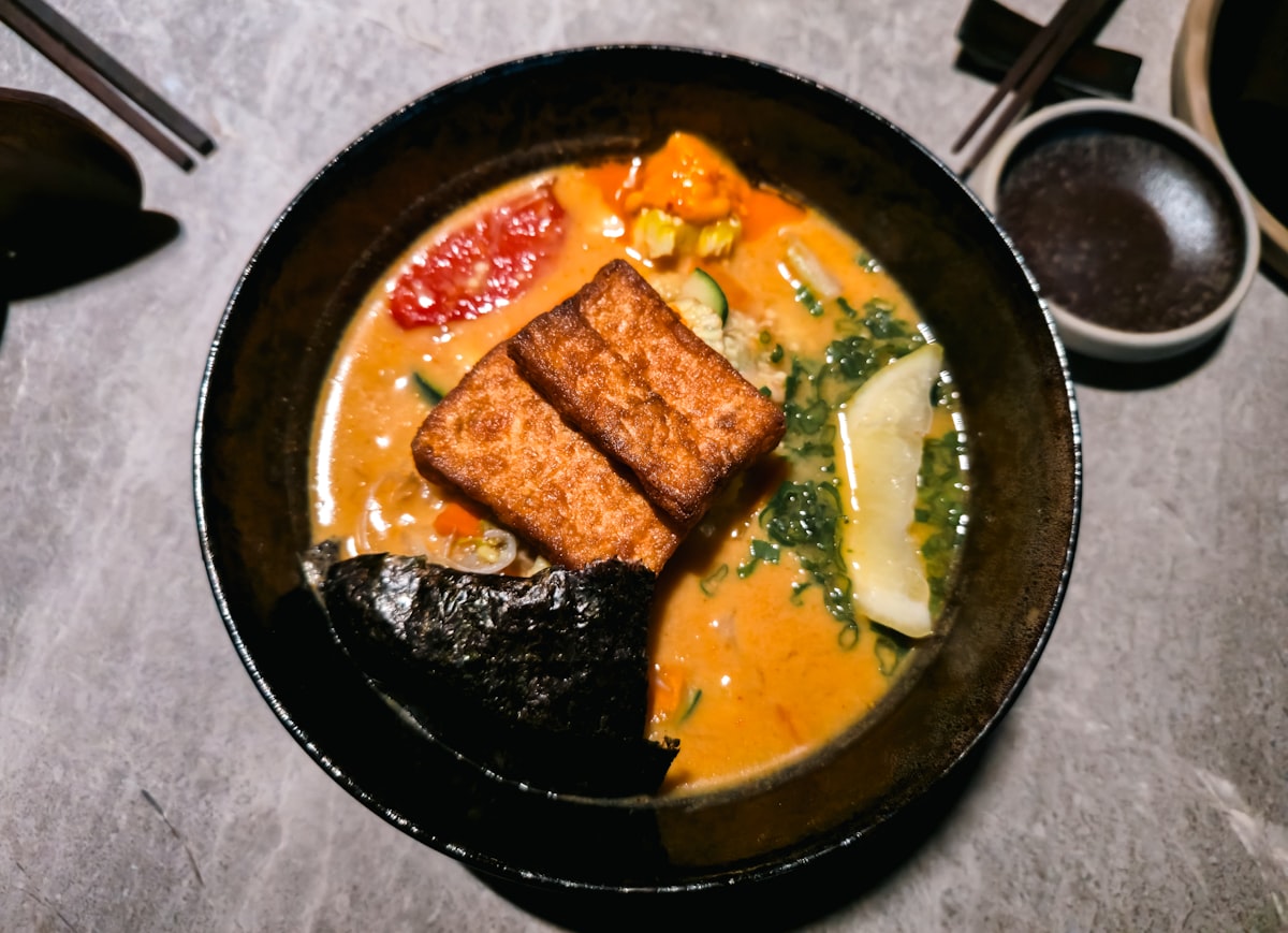 A golden coconut curry noodle bowl topped with crispy tofu, nori, and greens