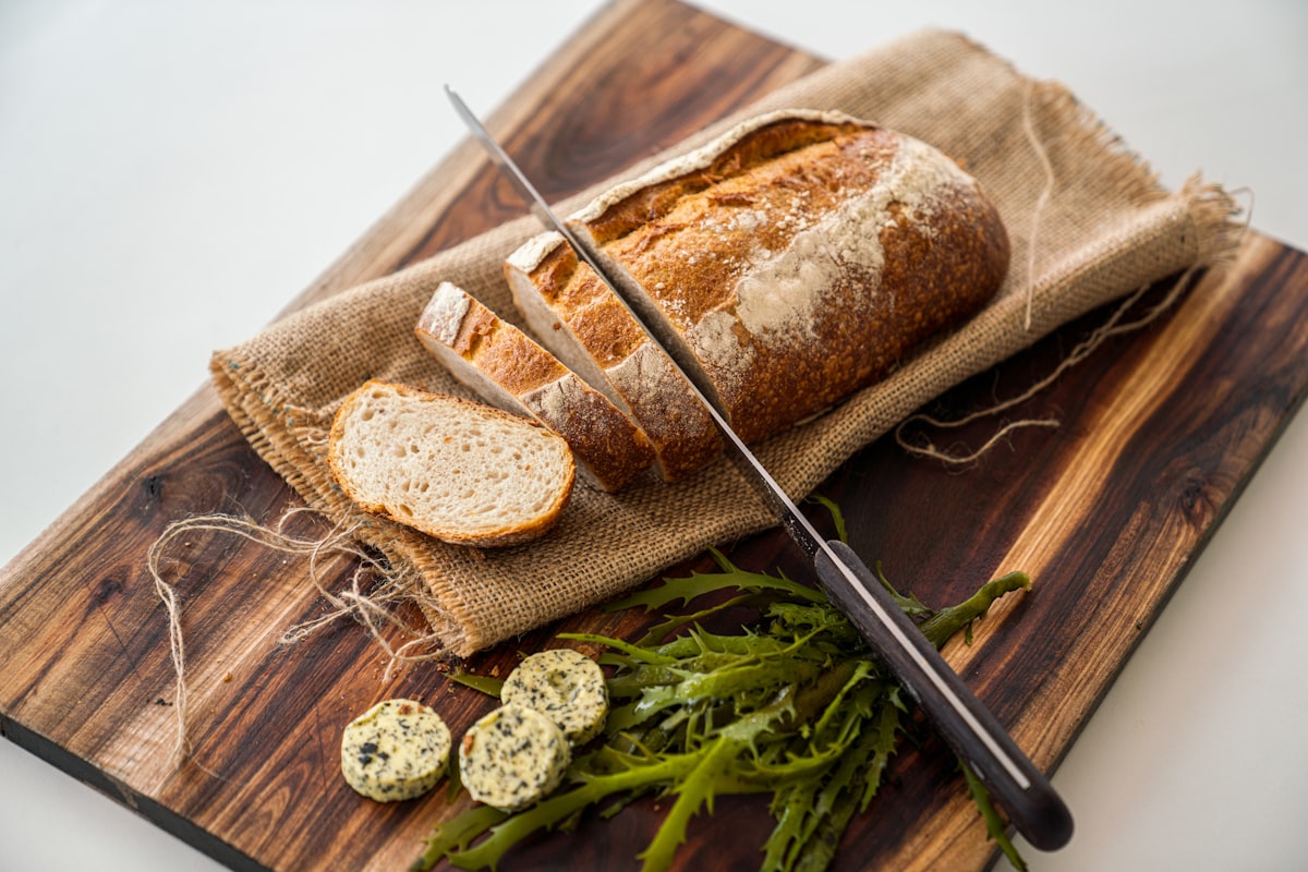A rustic loaf on a board beside coins of green-flecked herb butter