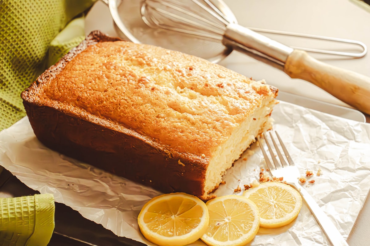 A sliced lemon loaf cake on a wooden board with a glaze drizzle