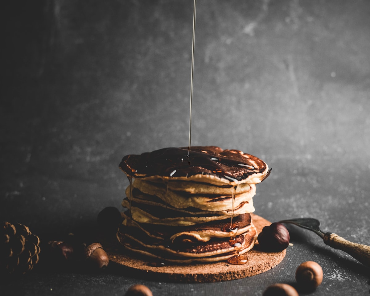 Syrup pouring over a tall stack of pancakes