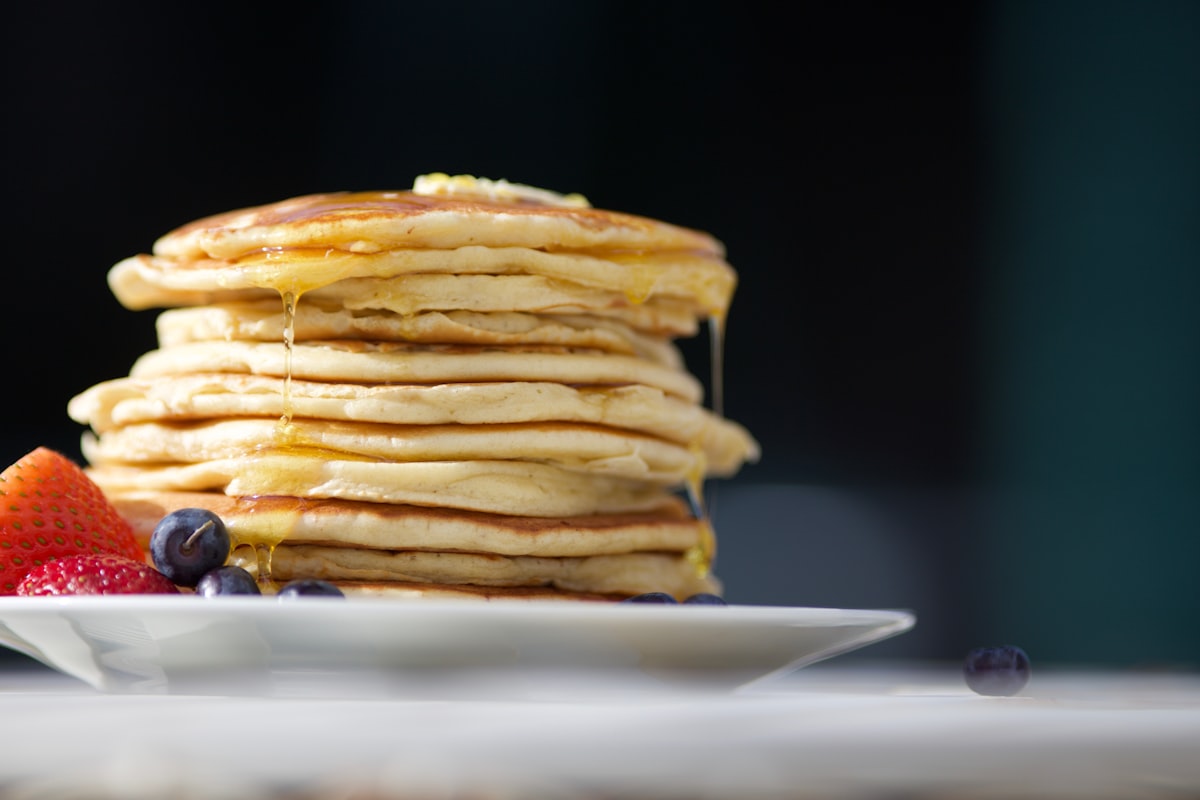 A tall stack of golden pancakes with butter melting on top and syrup running down the side