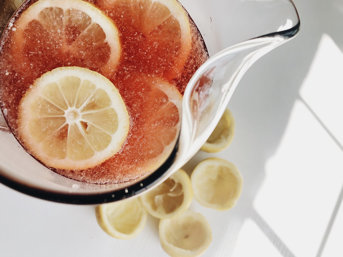 A glass pitcher of pink strawberry lemonade with lemon slices and ice