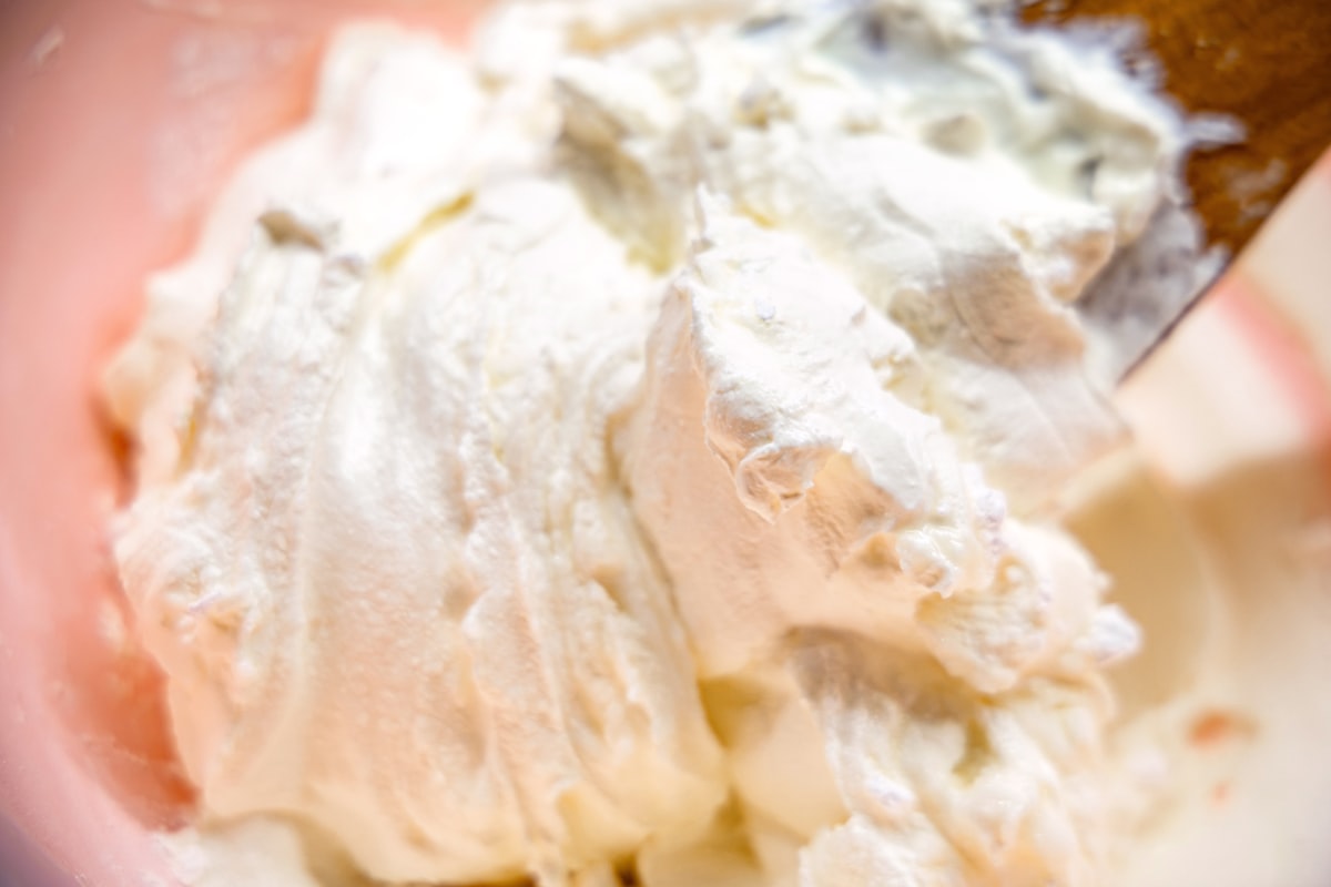 A wooden spoon folding thick whipped cream in a pink bowl