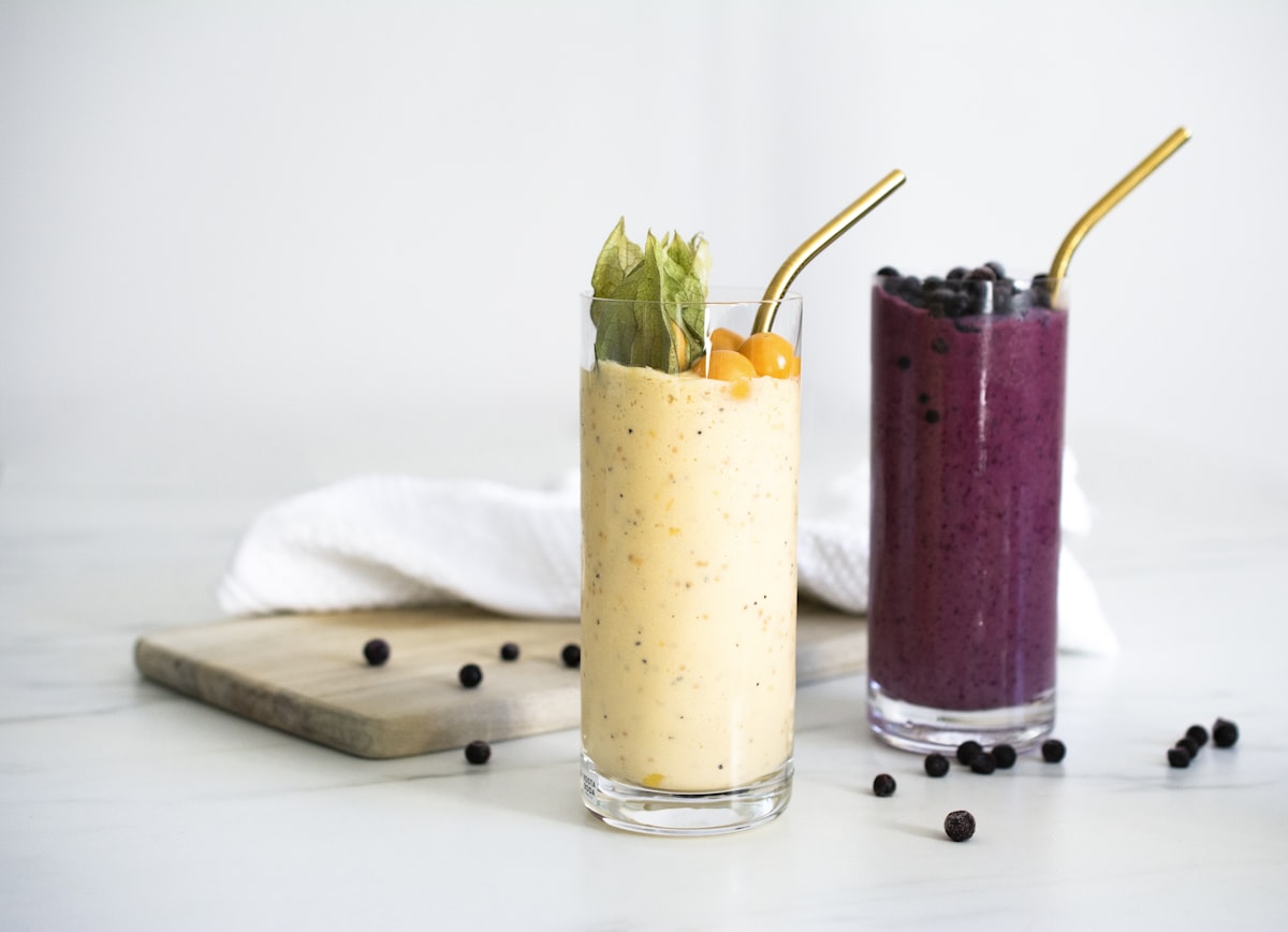 A tall golden mango smoothie with a coconut rim on a bright counter