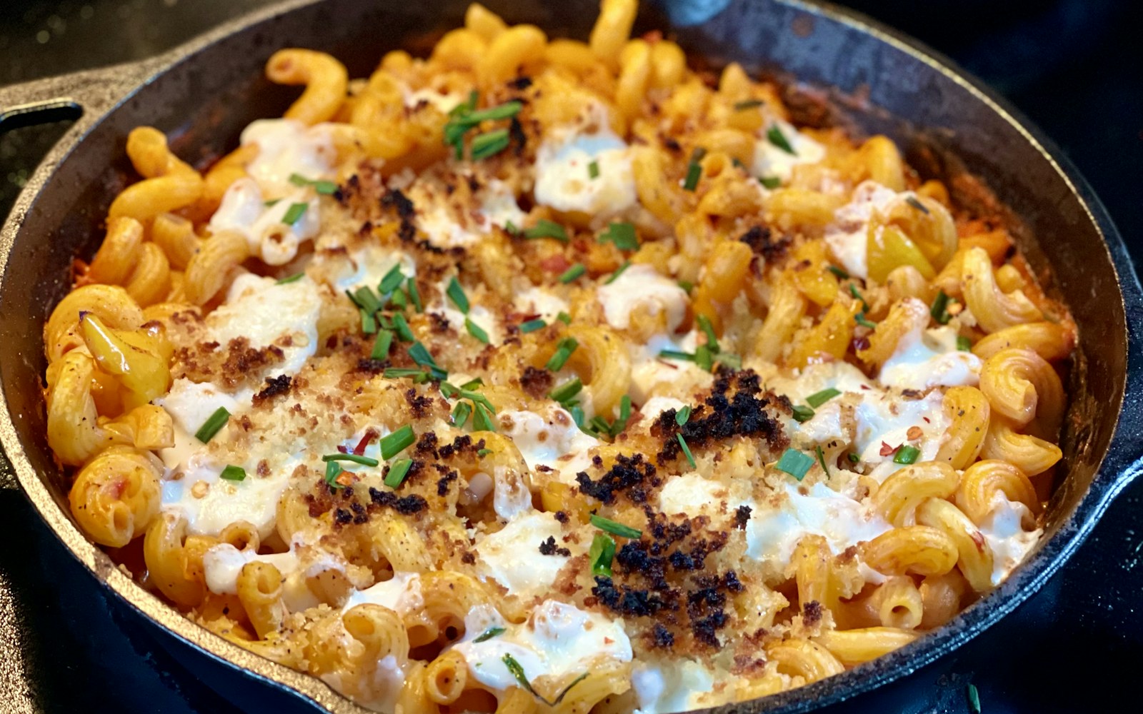 A cast-iron skillet of baked macaroni and cheese scattered with herbs