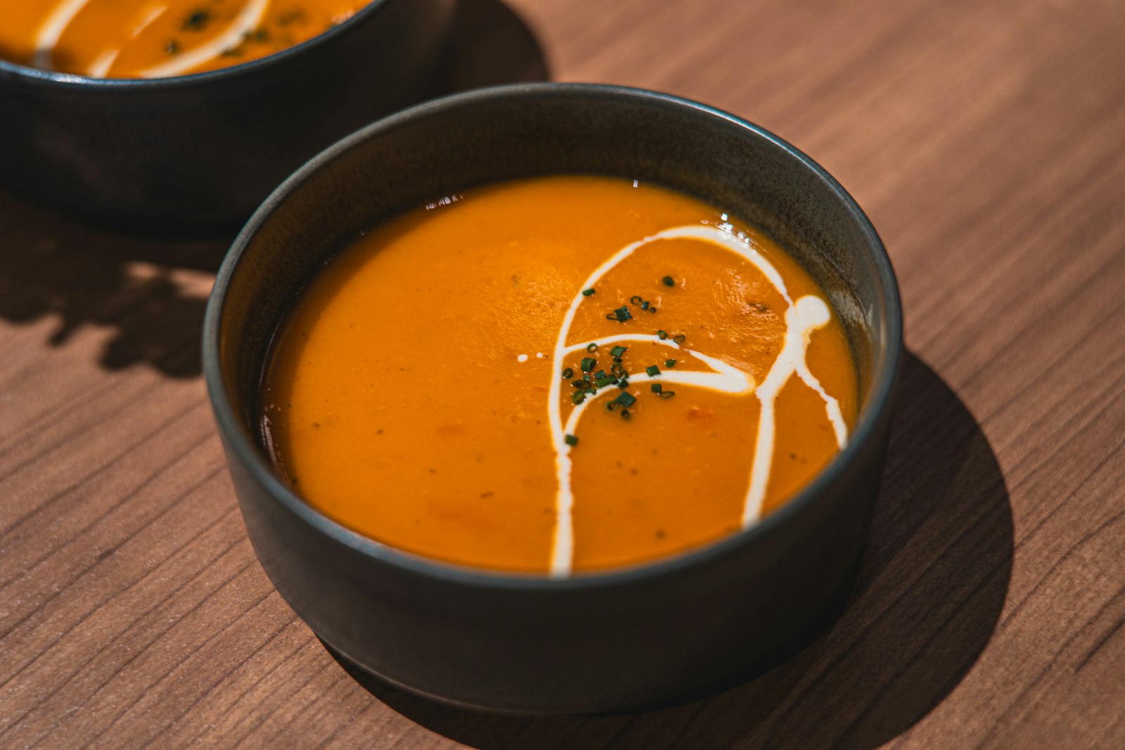 A dark bowl of smooth orange pumpkin soup with a white cream swirl on a wooden table